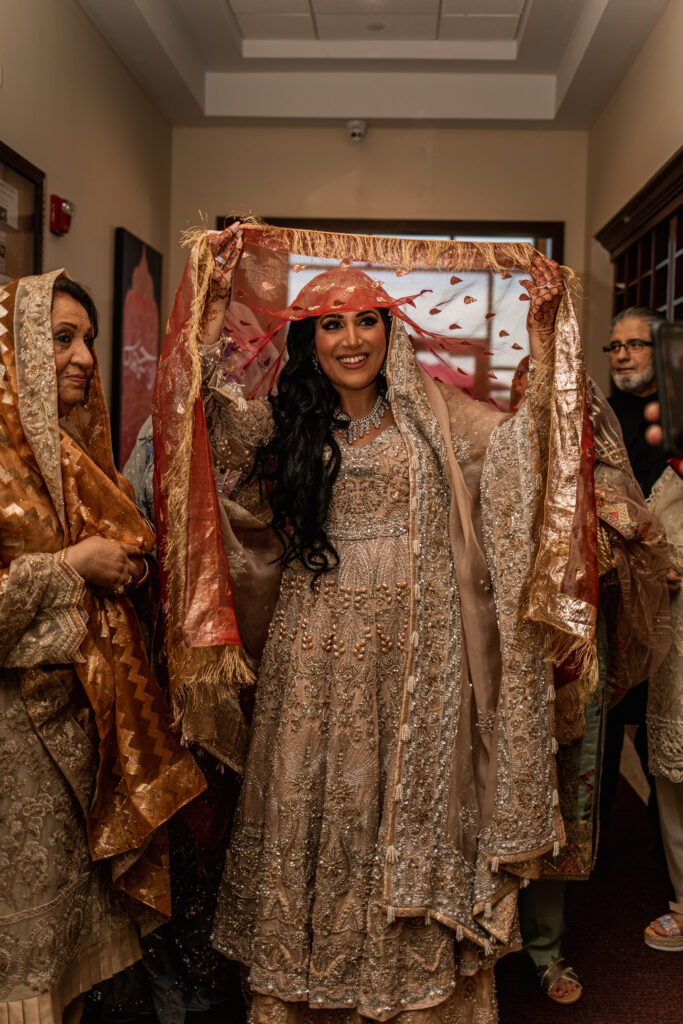Bride standing under a veil, surrounded by loved ones, as she prepares for the ceremony.