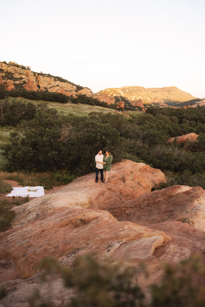 A couple stands on a rocky trail, holding hands and smiling, surrounded by the natural beauty of South Valley Park.