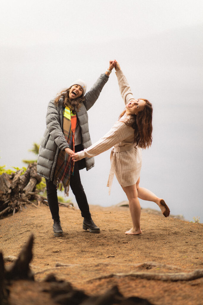 Joyful Twirl: Cassie and her friend twirling and laughing together at Crater Lake, enjoying the moment post-engagement.

