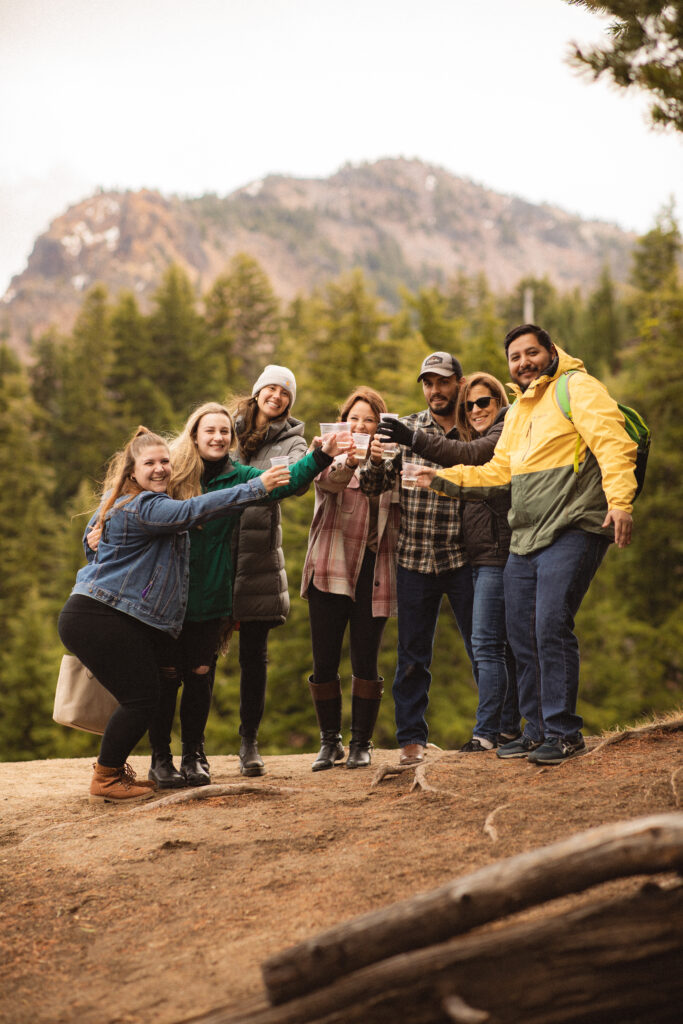 Group Celebration: Cassie, Ronnie, and their friends posing for a group photo, celebrating the engagement at Crater Lake with mountains in the background.

