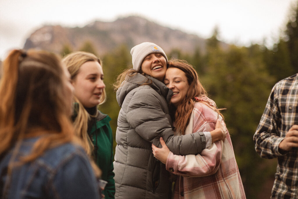 Hugs and Happiness: Cassie hugging her friend tightly, both wearing warm jackets, sharing a moment of happiness after the proposal.

