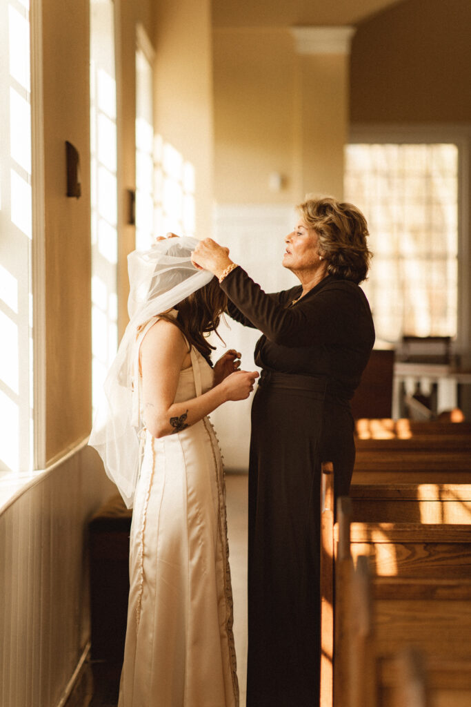 Bride getting ready with assistance from a family member, capturing a heartfelt moment.
