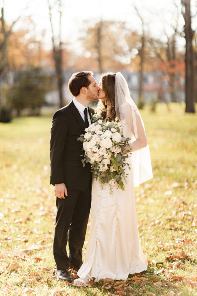 Bride and groom kissing in the autumn sunlight, showcasing the beauty of their small, intimate wedding.
