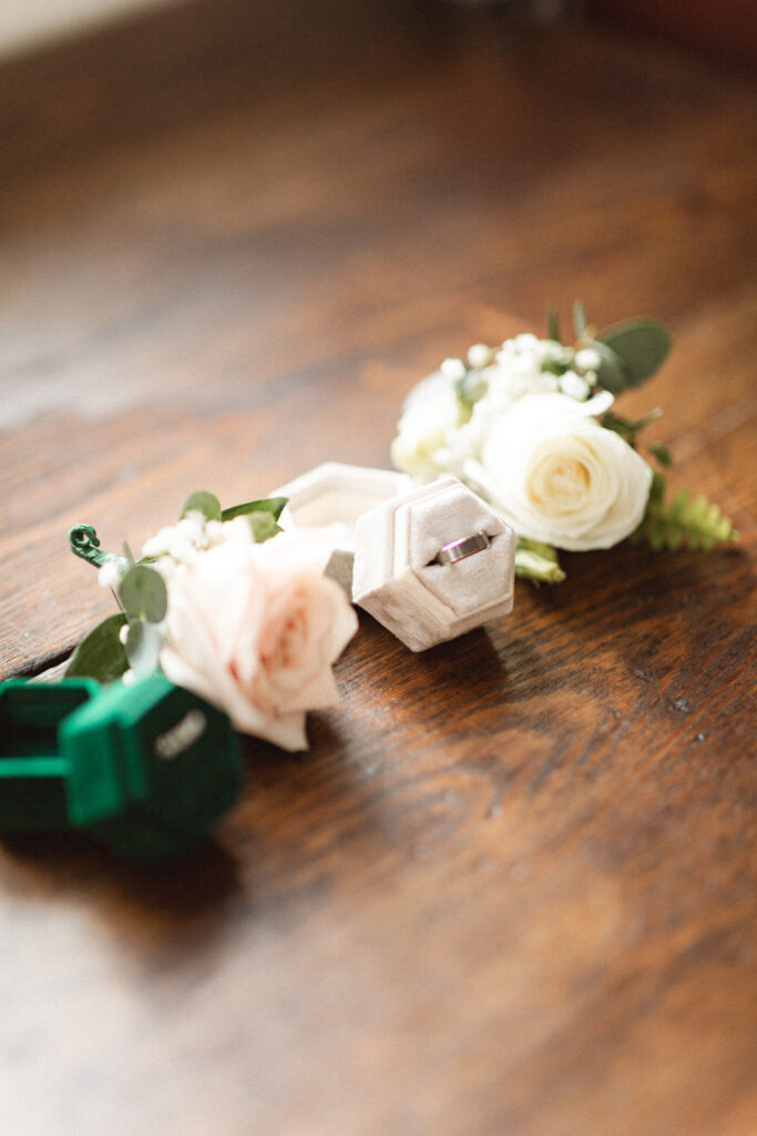 Close-up of wedding rings and boutonnieres on a wooden table, highlighting unique elopement photography.
