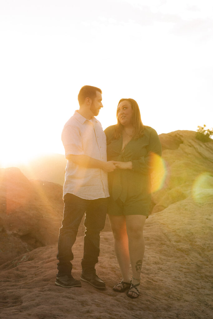 The couple holds hands, silhouetted by the setting sun, casting a golden glow over the landscape.
