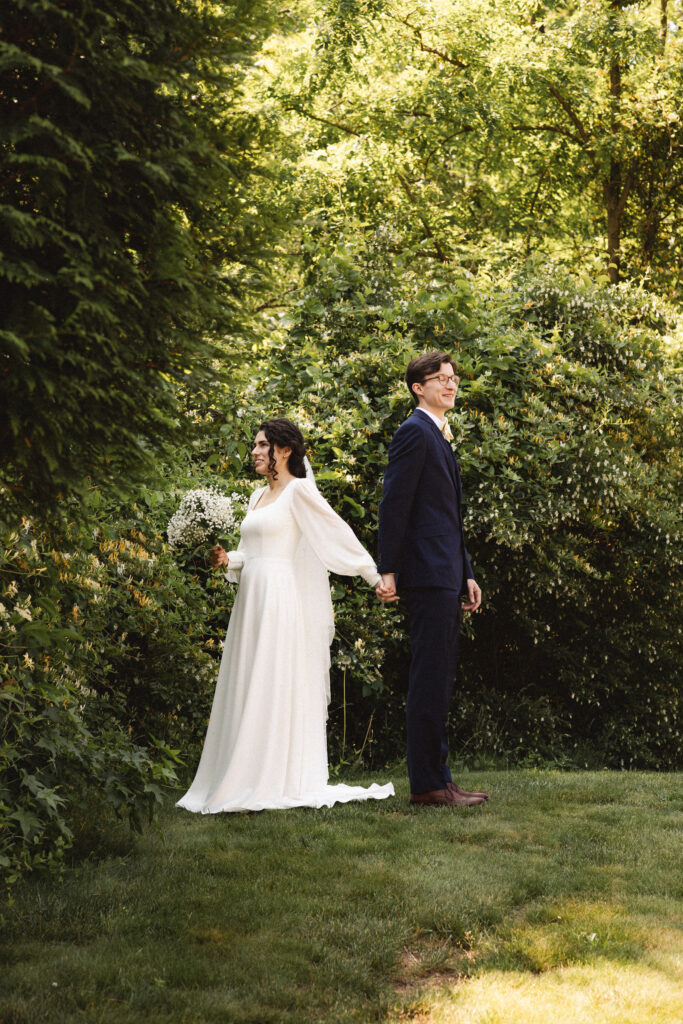 Bride and groom standing together, surrounded by lush greenery.
