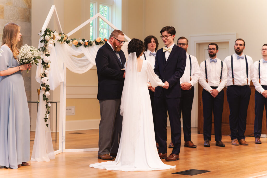 Bride and groom holding hands, standing with the officiant during the ceremony.
