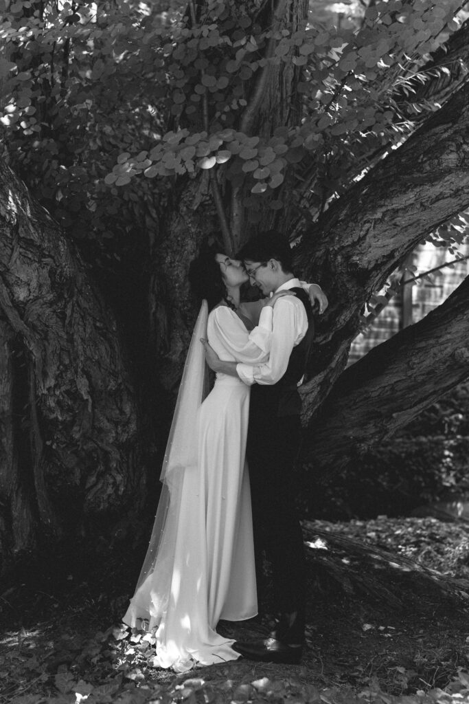 Bride and groom sharing a kiss under a large tree.
