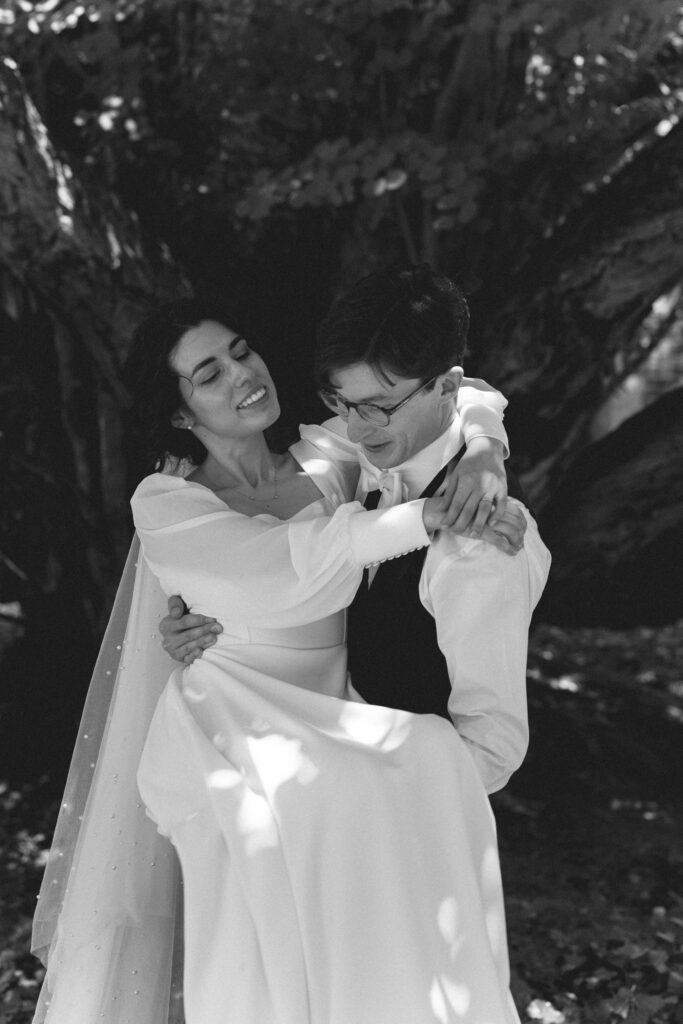 Bride and groom in a playful moment under a tree, the bride laughing.
