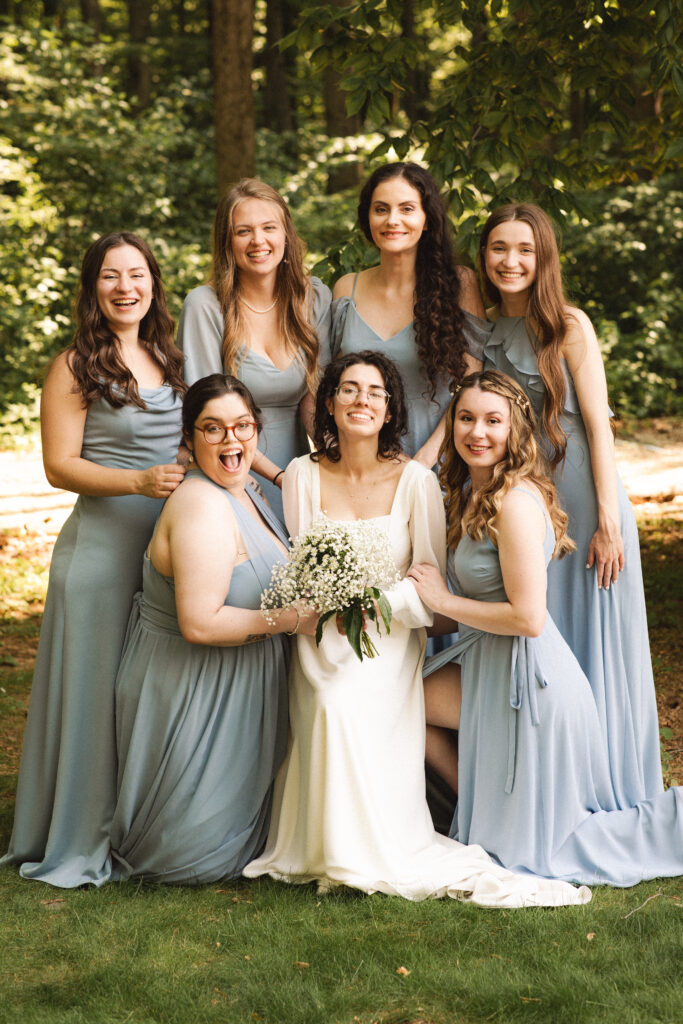 Bride surrounded by bridesmaids in pastel dresses, all laughing together.
