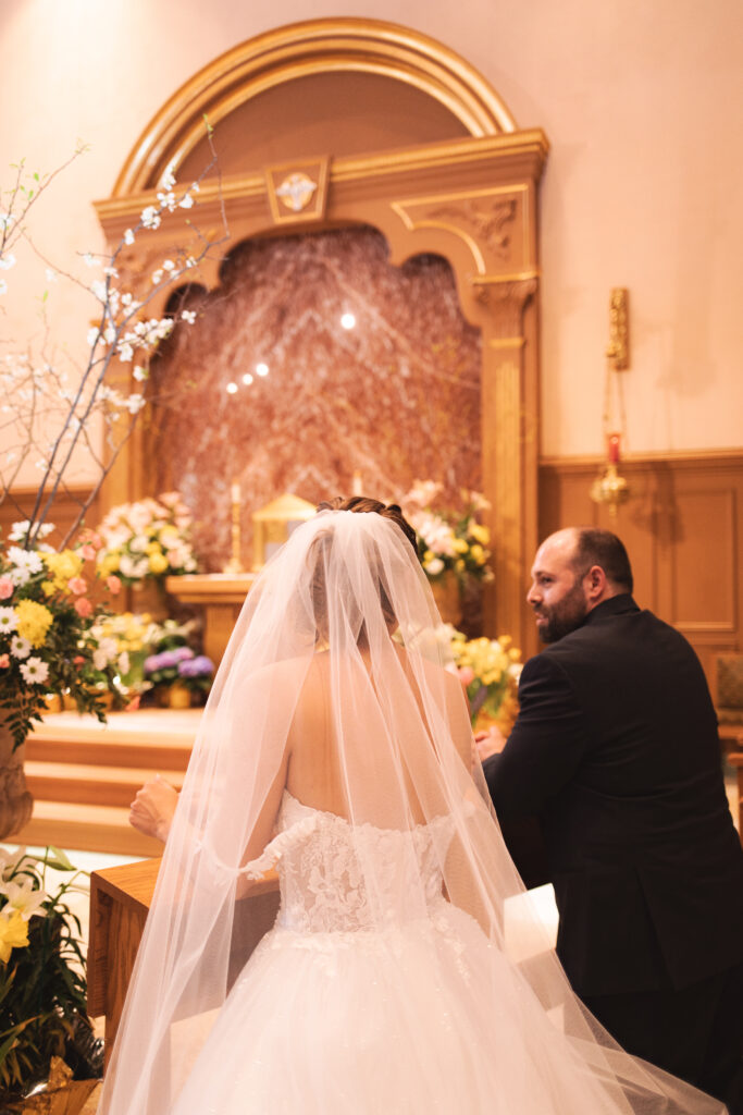 Briana and Pat kneeling at the altar, with Briana's veil cascading down.