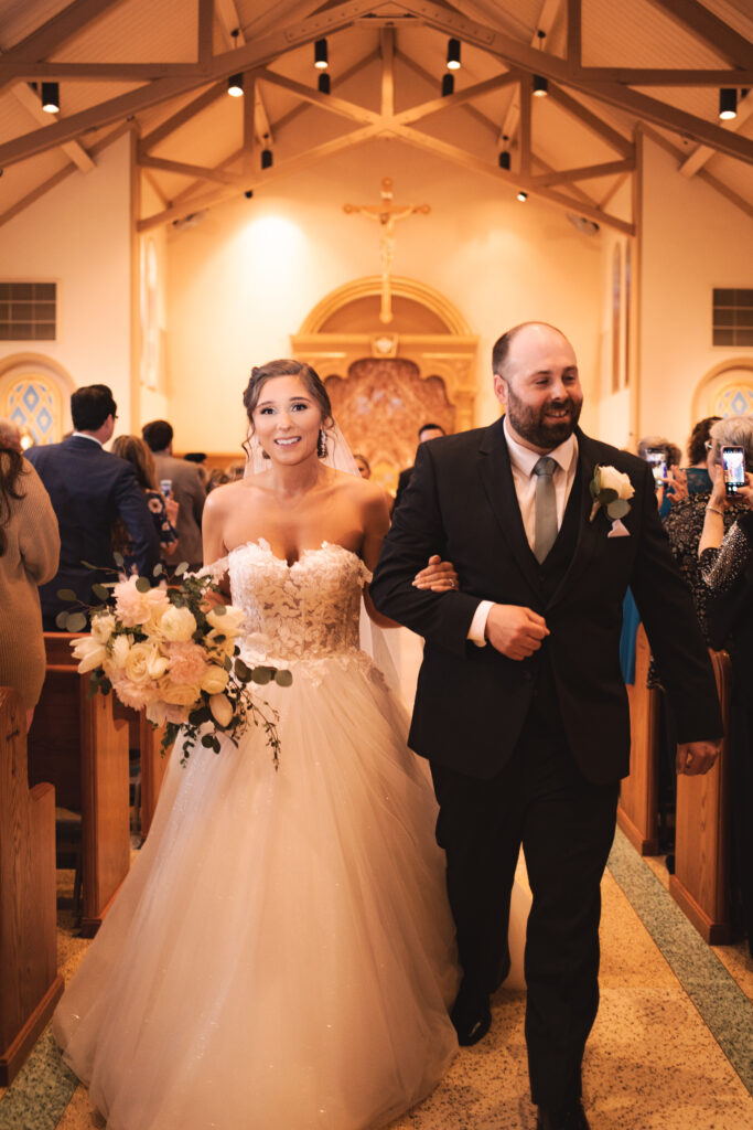 Briana and Pat walking down the aisle, with guests clapping and cheering.

