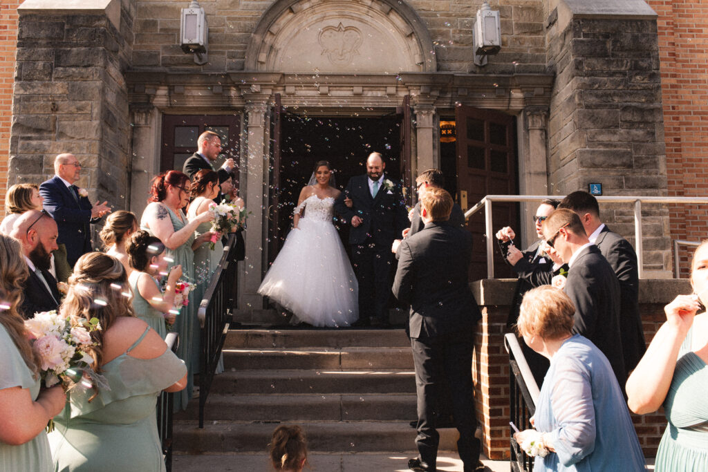 Briana and Pat exiting the church, greeted by guests blowing bubbles.