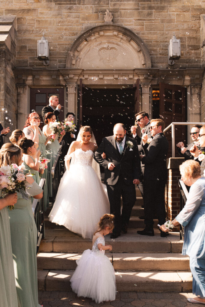 Briana and Pat exiting the church, with their bridesmaids and groomsmen cheering them on.

