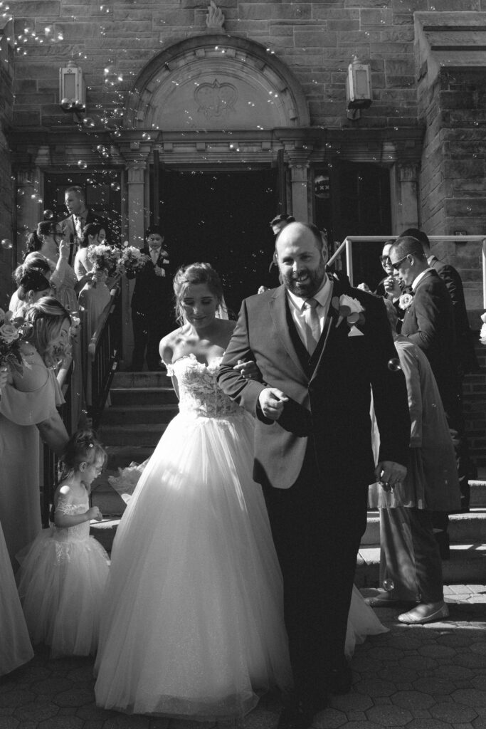 Black and white photo of Briana and Pat exiting the church, with confetti falling around them.