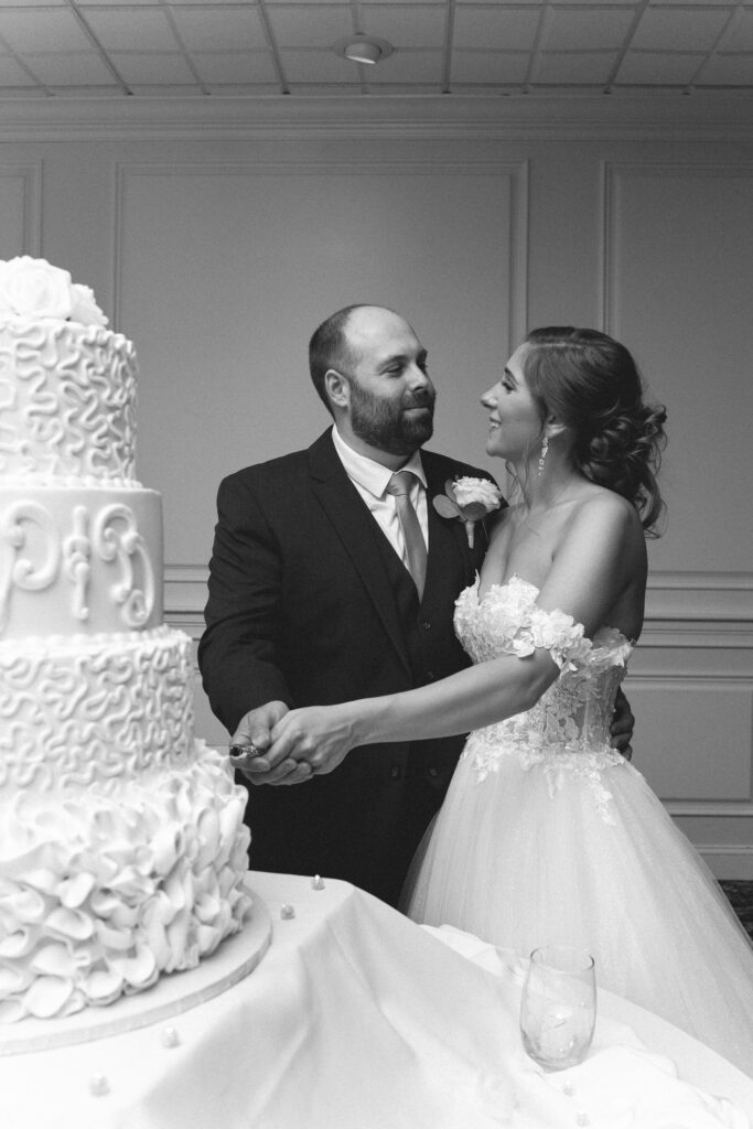 Briana and Pat smiling at each other while cutting their wedding cake.

