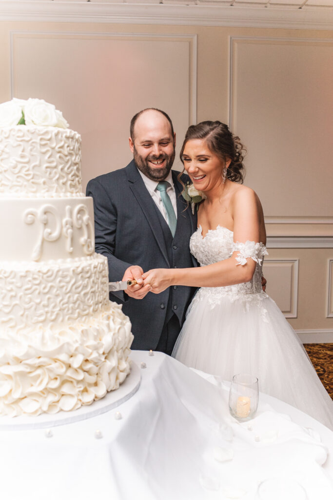 Briana and Pat standing next to their three-tiered wedding cake, ready to cut it.

