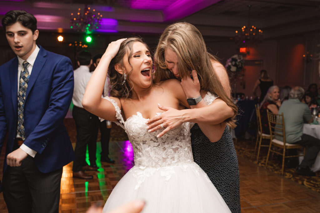 Briana laughing and dancing with a guest during the wedding reception, with other guests dancing in the background.