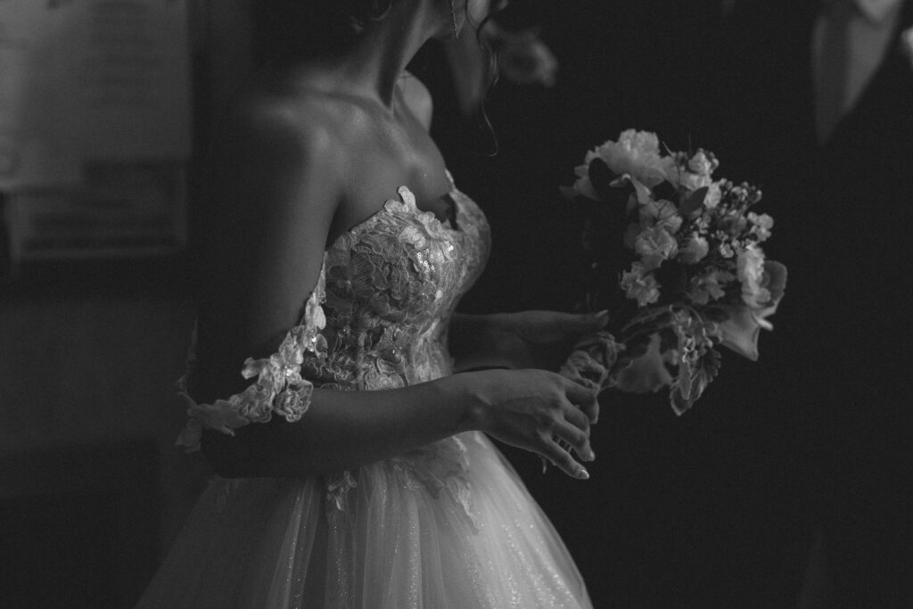 Black and white close-up of Briana holding her bouquet, showcasing the intricate details of her wedding dress.