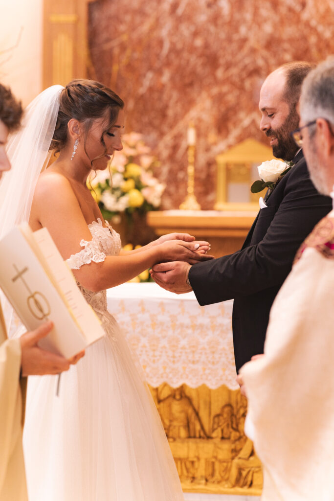  Briana and Pat during the ring exchange at the altar, with the priest officiating.

