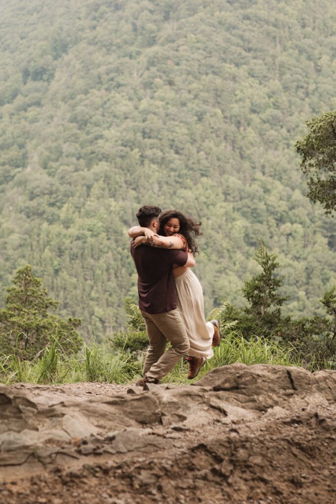 Alec lifts Jac in celebration, the couple exuding happiness with the picturesque valley as their backdrop.

