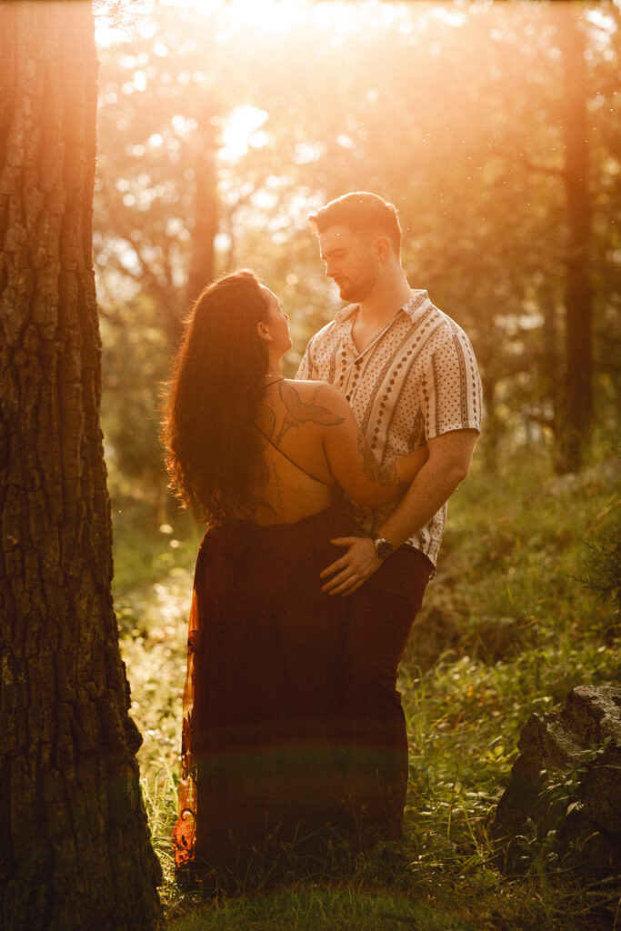 Jac and Alec walk hand in hand along a wooded path, the sunlight creating a dreamy, ethereal effect.

