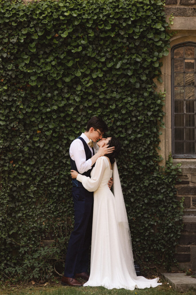 Bride and groom embracing in front of a vine-covered wall.
