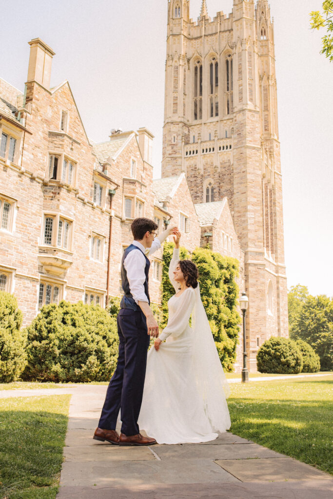 Bride and groom holding hands, facing each other in front of a cathedral.