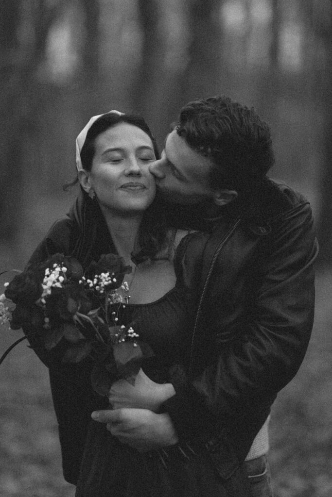 Black and white photo of a couple in a loving embrace in the woods.
