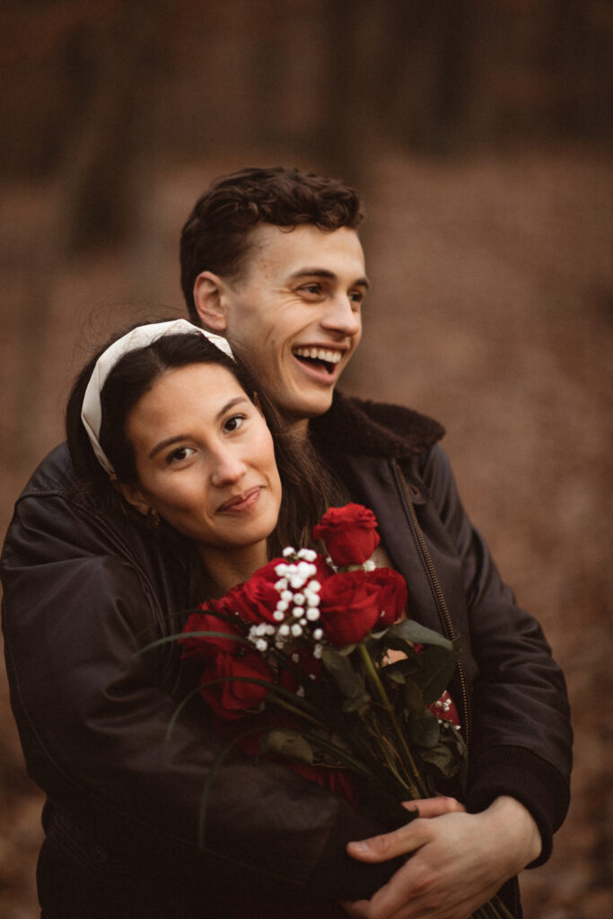 Couple embracing with smiles, the woman holding a bouquet of roses.
