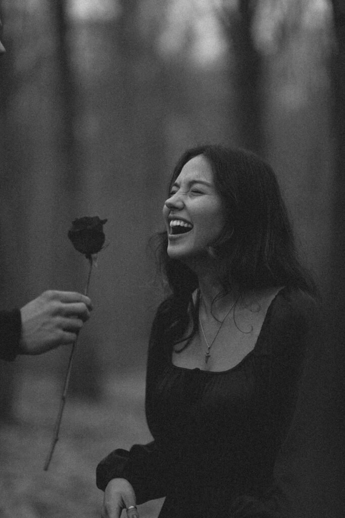 Black and white photo of a woman laughing while holding a single rose.
