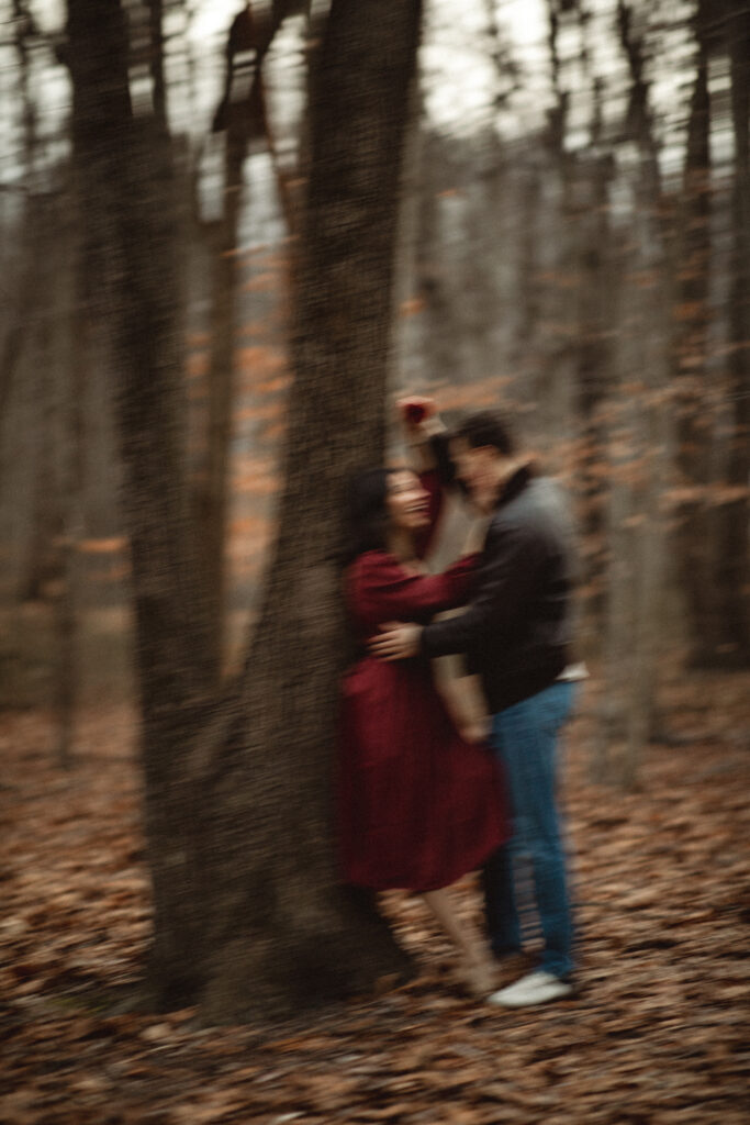 Couple embracing tenderly in the woods, leaning against a tree.
