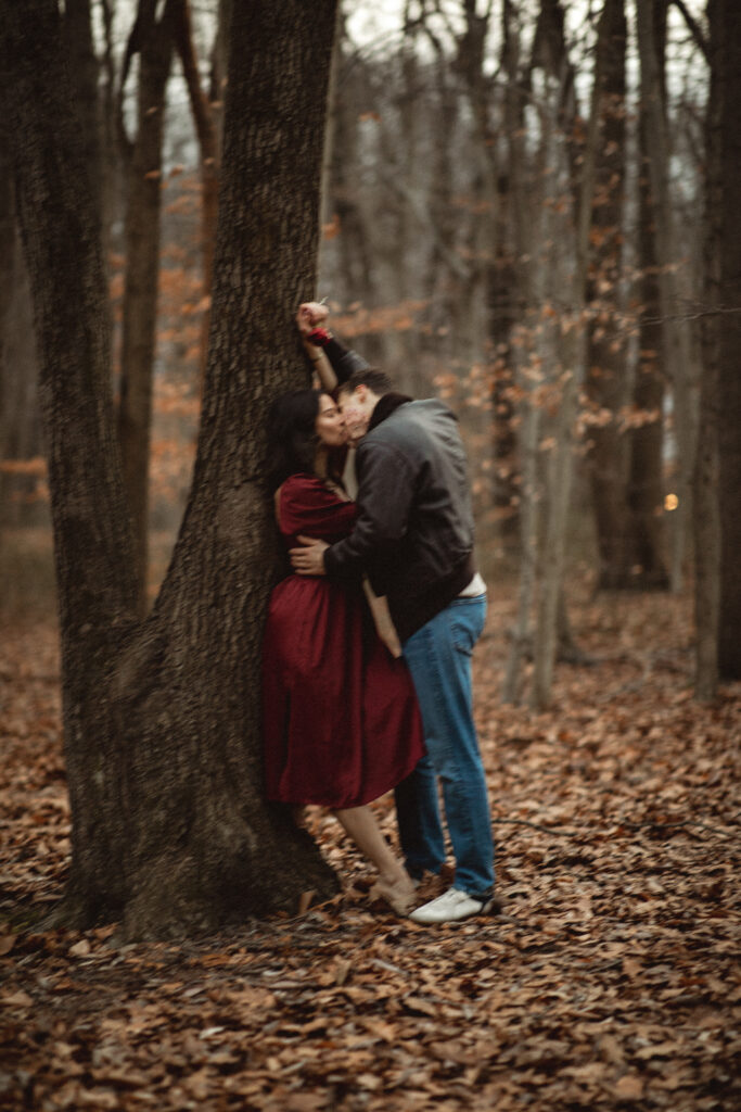 The beautiful couple kissing, holding hands, with the woman with her back to the tree.
