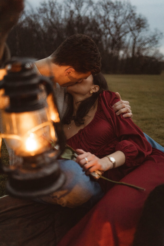 Couple snuggling on a blanket in a field, surrounded by lanterns and flowers.