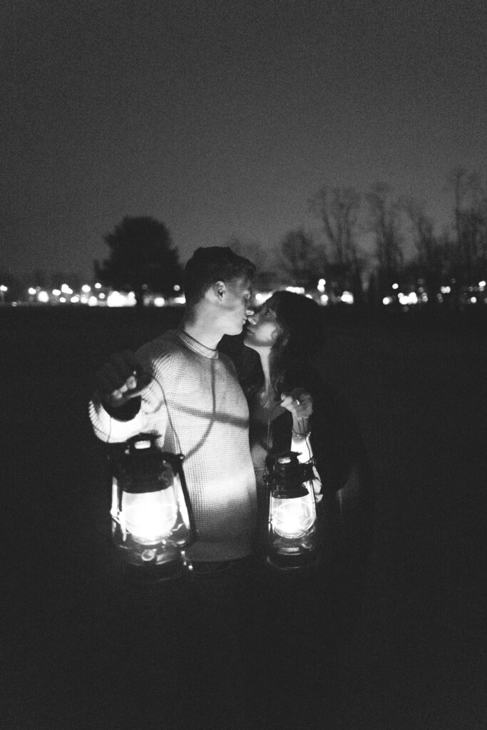 Black and white photo of a woman holding lanterns, walking through a field at night.