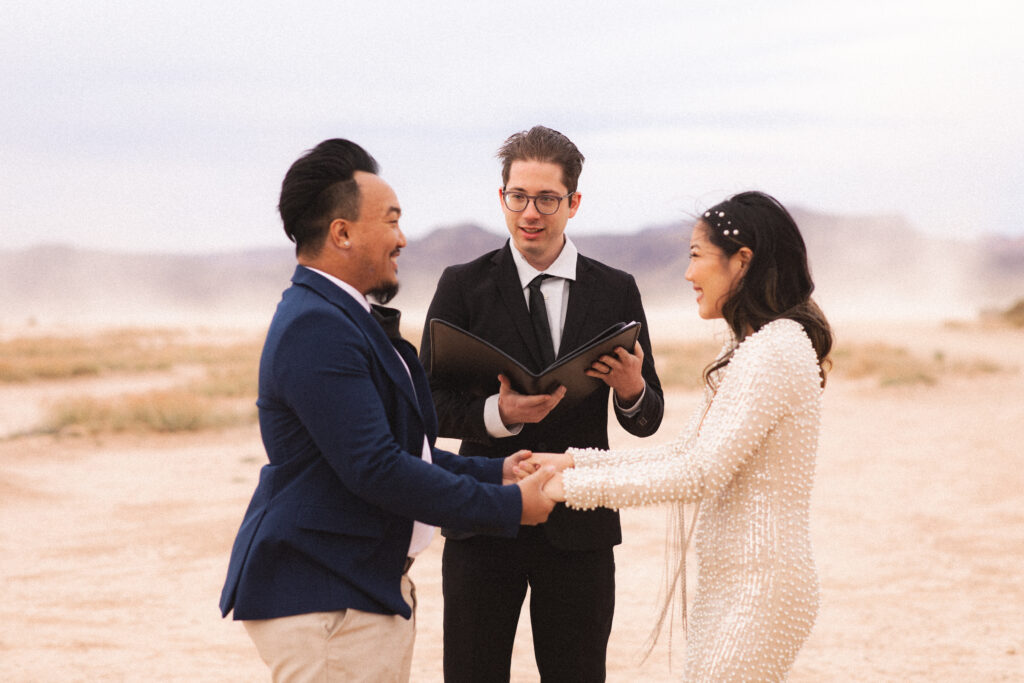 Bride and groom exchanging vows with an officiant, a small wedding ceremony in the desert.
