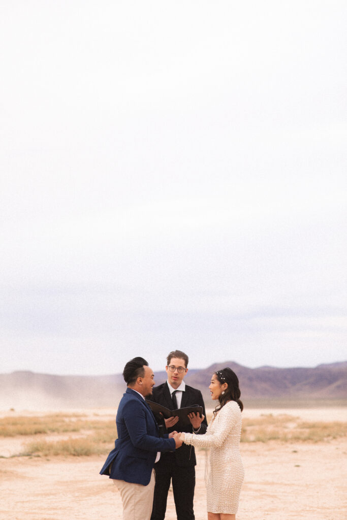 Bride and groom exchanging vows with an officiant, a small wedding ceremony in the desert.
