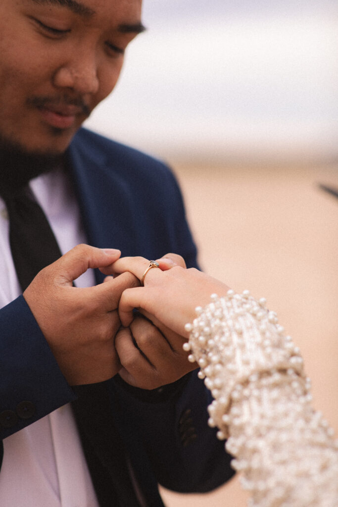 Close-up of the groom placing a ring on the bride’s finger, an intimate wedding photography moment.
